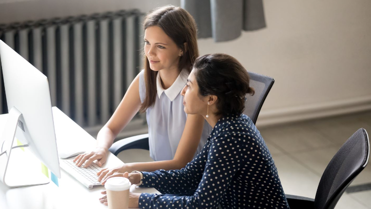 Two businesswoman working and having coffee while collaborating on project and sharing computer.